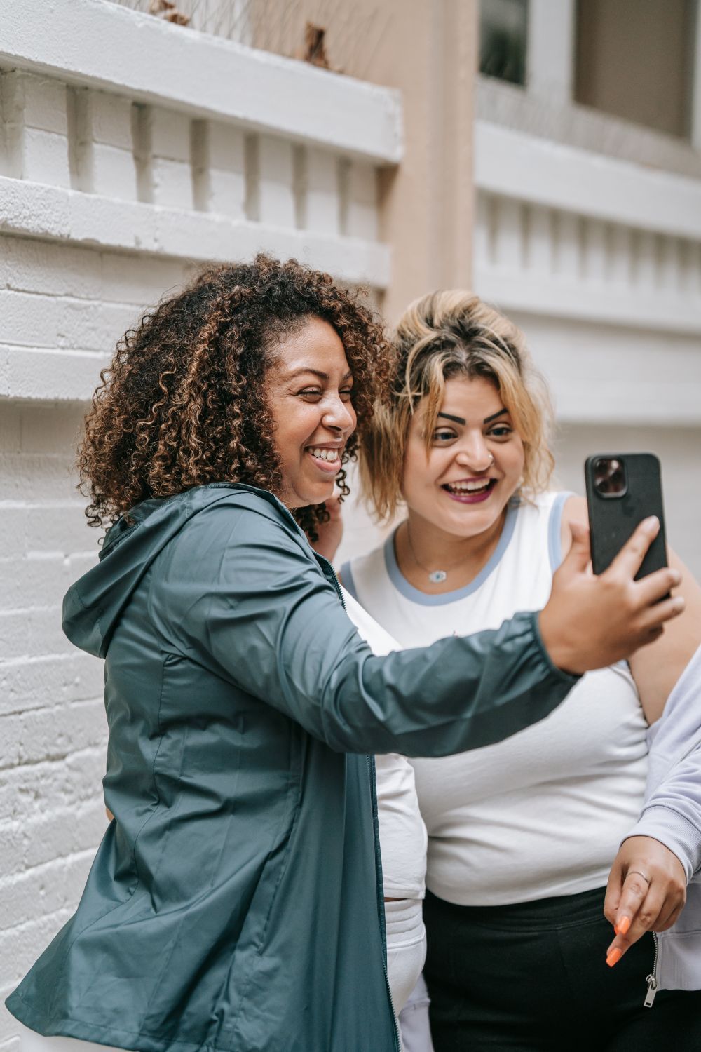 Dos amigas se hacen un selfie junto a una pared de ladrillo.