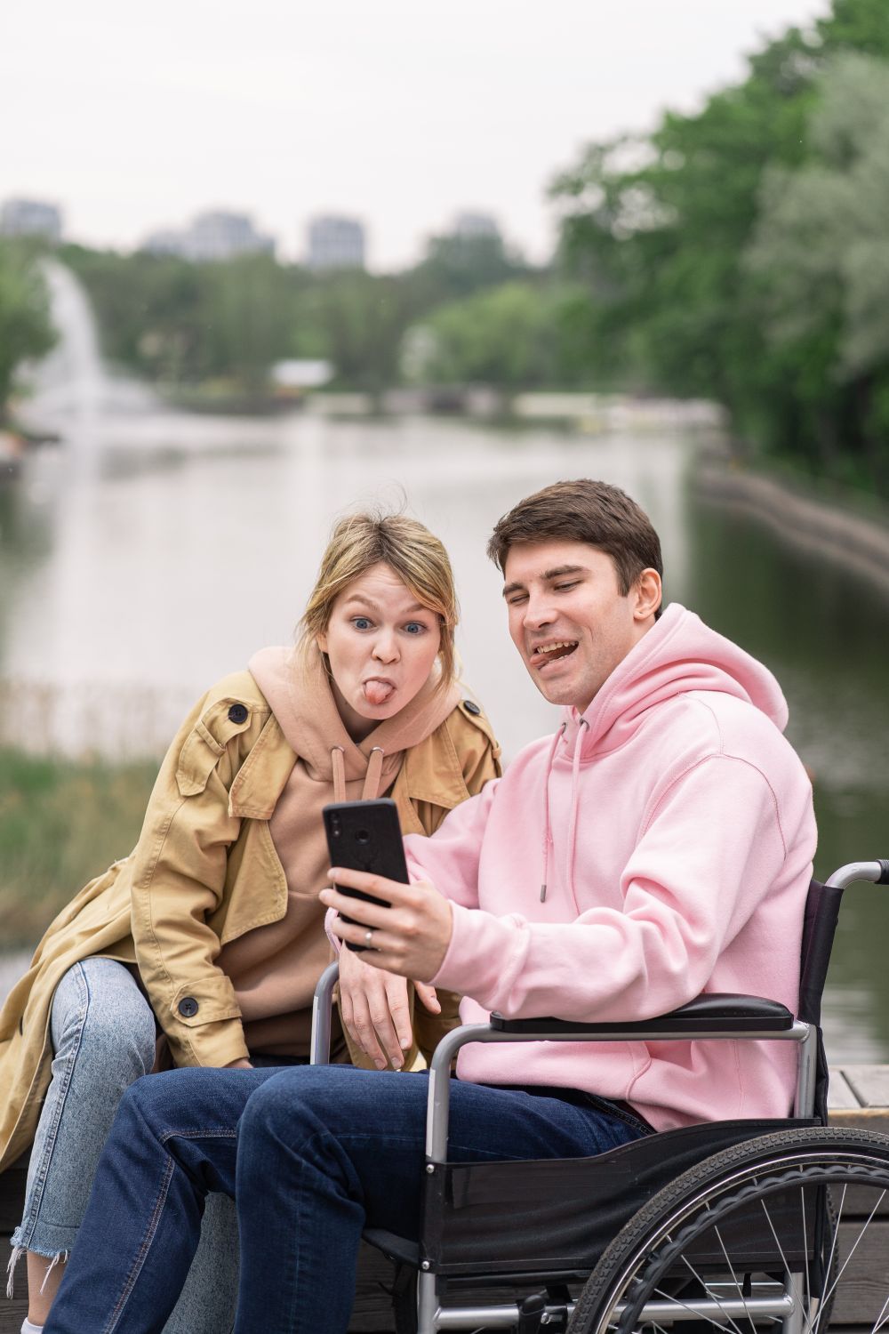 Una pareja se hace un selfie junto a un lago; él va en silla de ruedas.